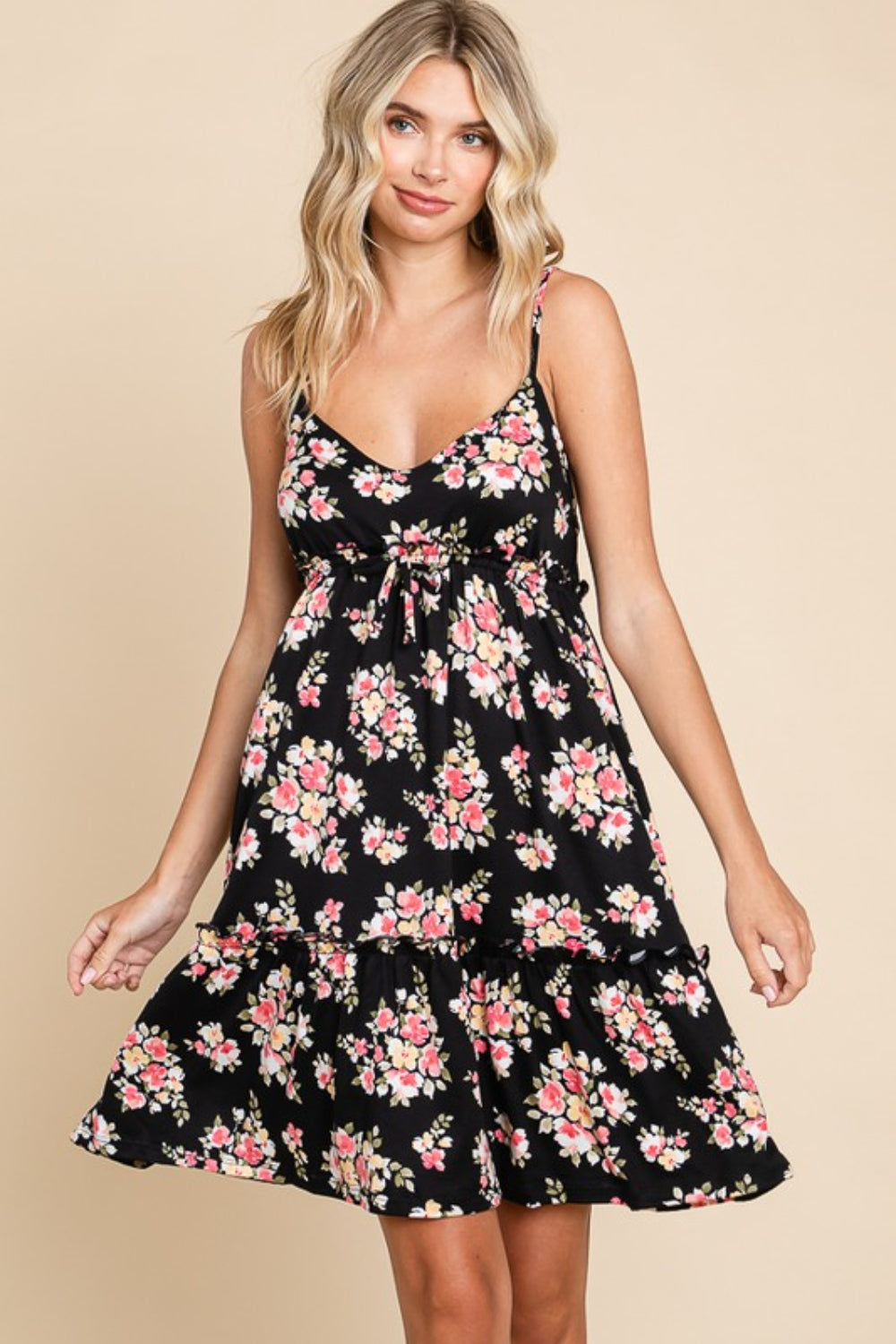 A woman poses against a beige background, modeling the Culture Code Full Size Floral Frill Cami Dress, featuring a black floral print and delicate frilled detailing at the hem.