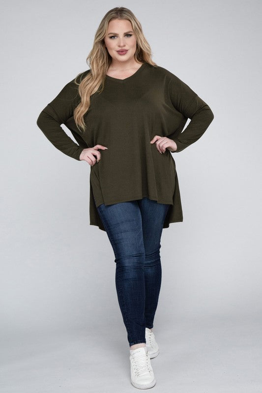 A woman with long, blonde hair wears a Plus Dolman Sleeve V-Neck Side Slit Hi-Low Hem Top and blue jeans, posing with one hand on her hip and smiling at the camera.