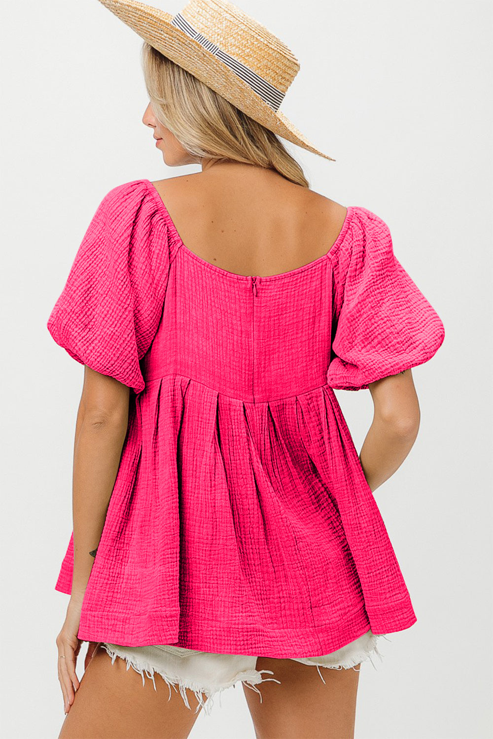 A woman wearing the BiBi Pleated Puff Sleeve Washed Blouse in pink, along with a wide-brimmed hat, strikes a pose against a beige background with one hand resting in her pocket.