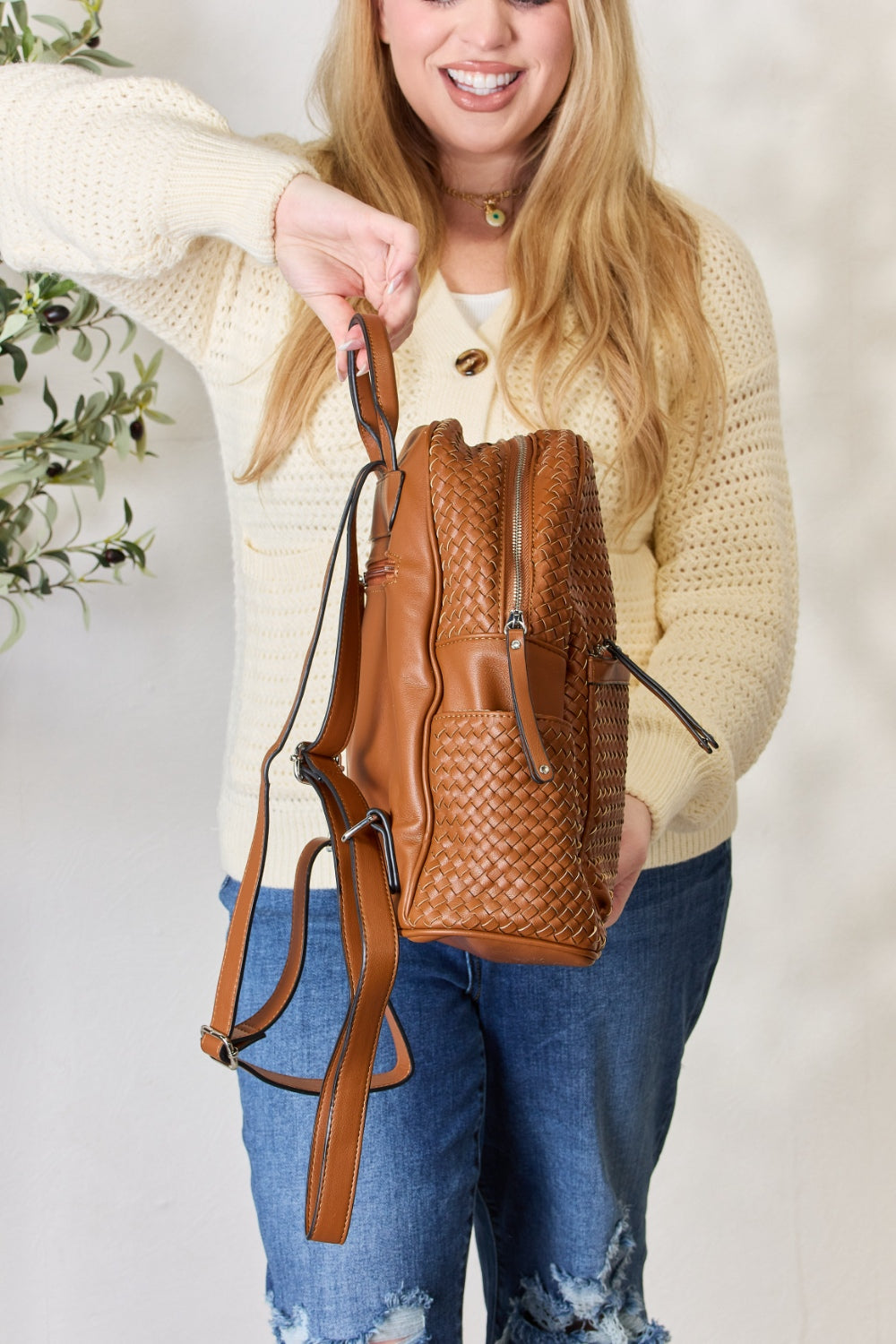 A person wearing a cream sweater and blue jeans carries the SHOMICO PU Leather Woven Backpack, showcasing exquisite craftsmanship with its woven design.