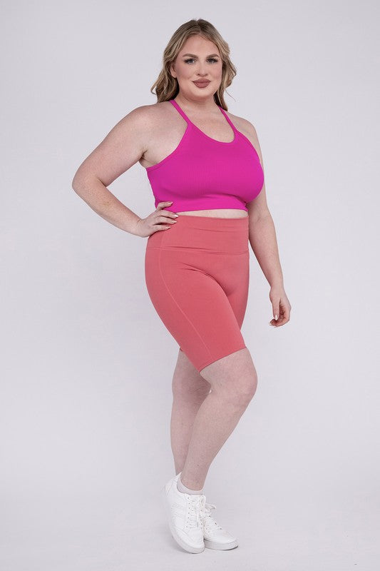 Against a plain background, a person showcases the Plus Athletic High Rise Biker Shorts in coral, crafted from high-quality athletic fabric and paired with a pink top.