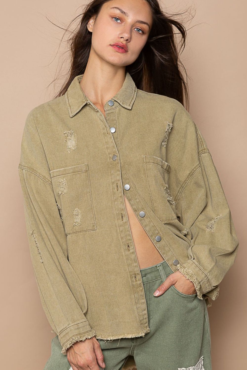 A woman with long hair wears a POL Button Down Raw Hem Distressed Shacket in khaki and matching pants, posing confidently against a beige background.