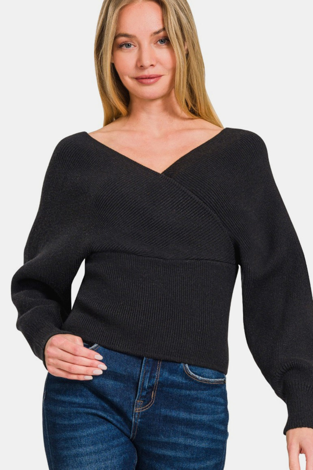 A woman stands against a plain white background, wearing the chic Zenana Cross Wrap Rib Long Sleeve Sweater in black paired with blue jeans.