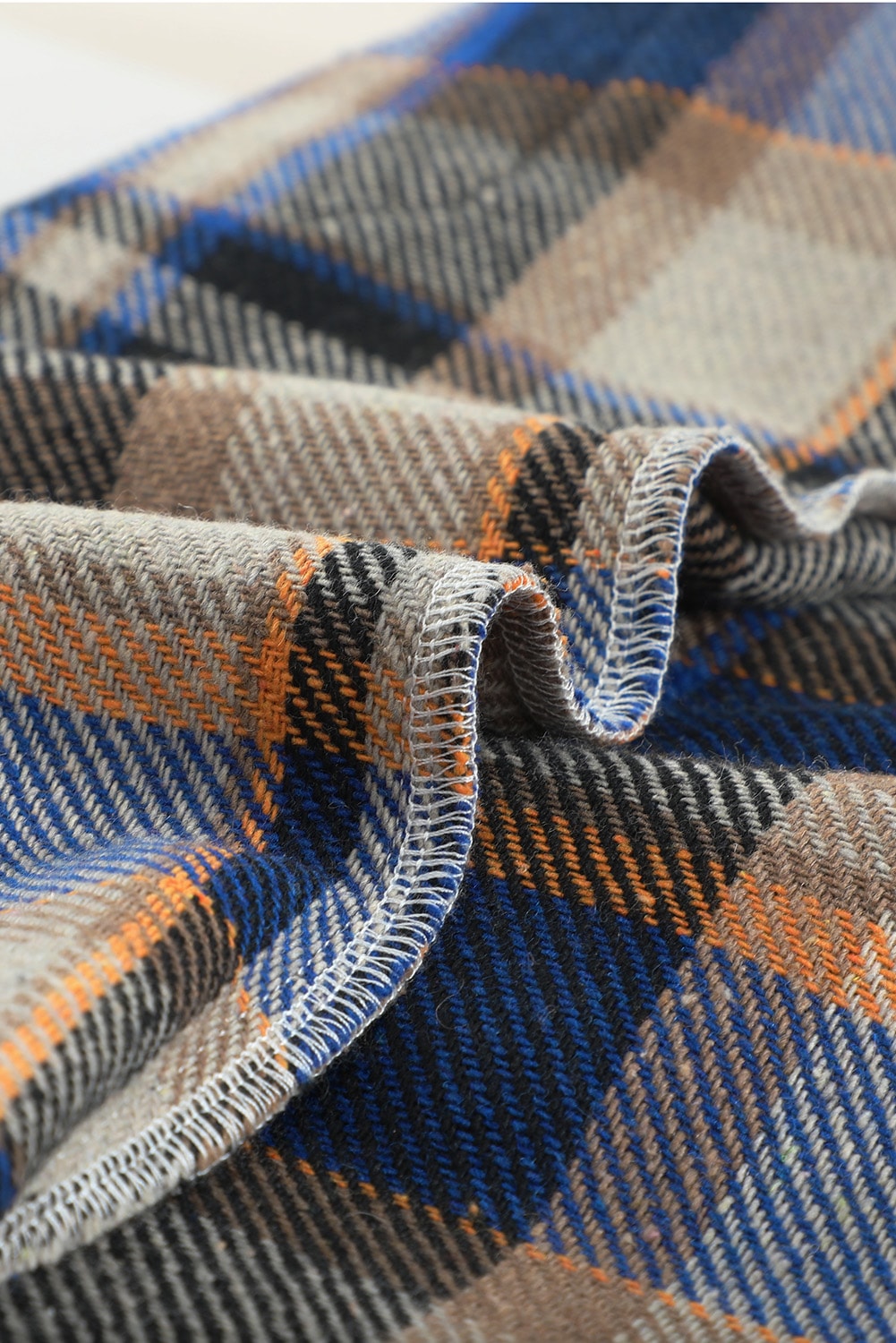 A person wearing a Brown Plaid Button Up Long Sleeve Flannel Shacket layered over a white top with ripped jeans and holding a brown handbag stands against a textured gray wall.