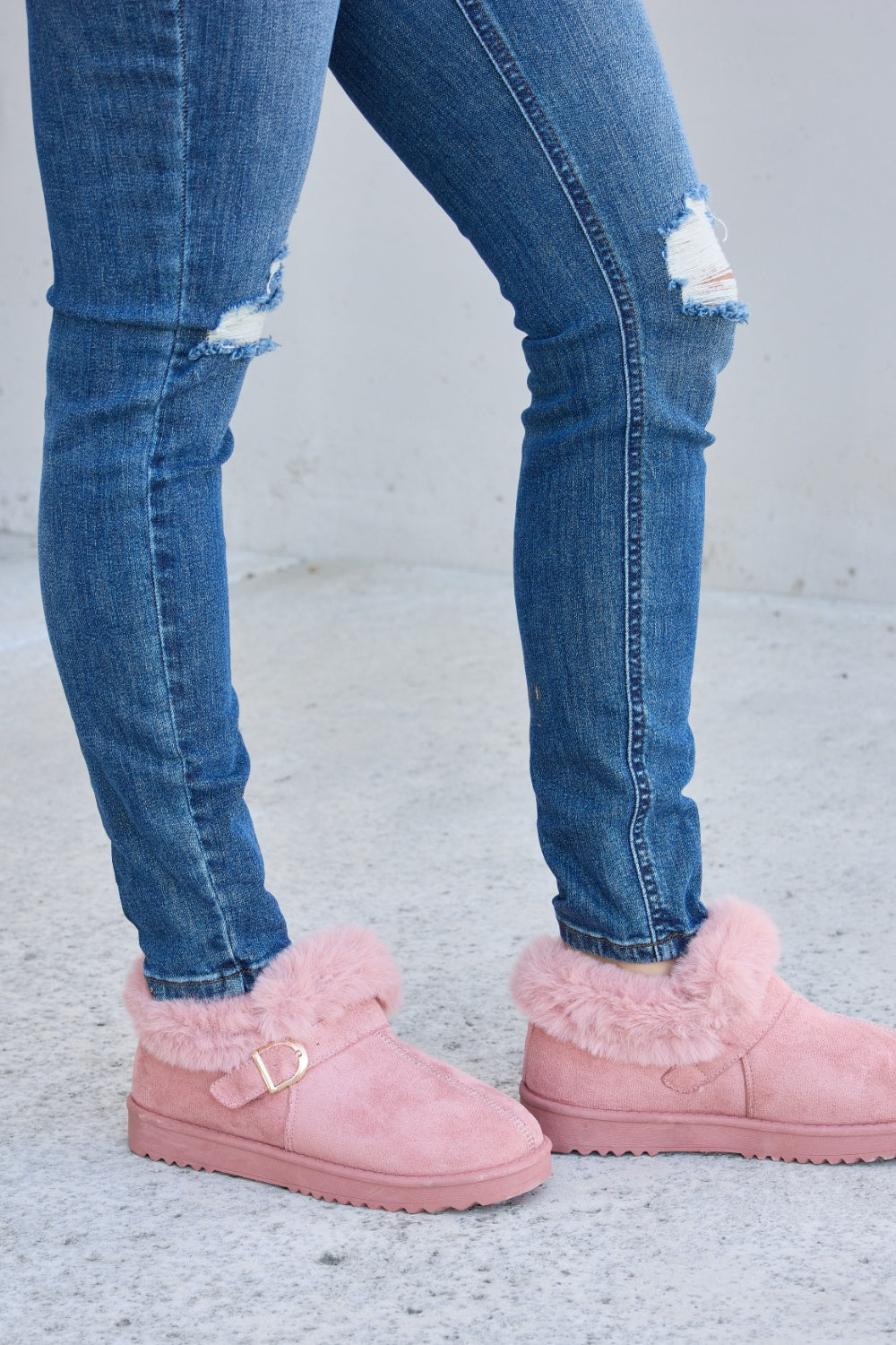 A person stands on a concrete surface, sporting ripped blue jeans and the Forever Link Furry Chunky Thermal Ankle Boots. The furry lining of these fashionable boots suggests both comfort and warmth for winter.