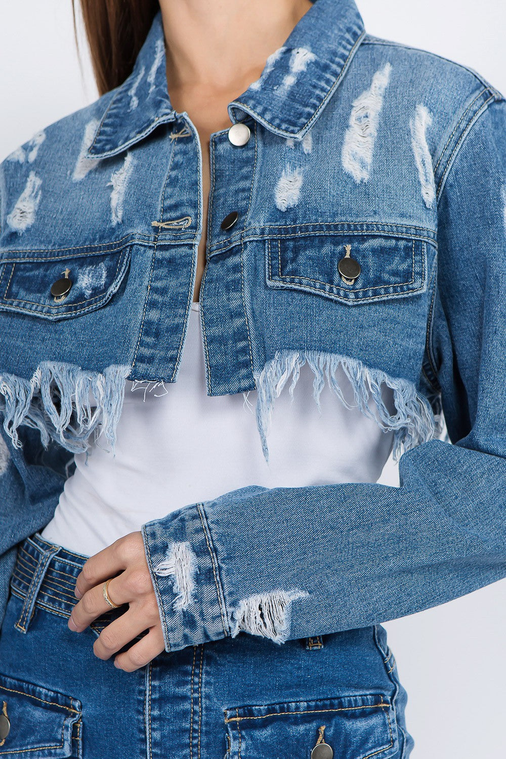 A woman wearing an American Bazi Distressed Denim Jacket with a frayed hem and matching skirt poses against a plain background.