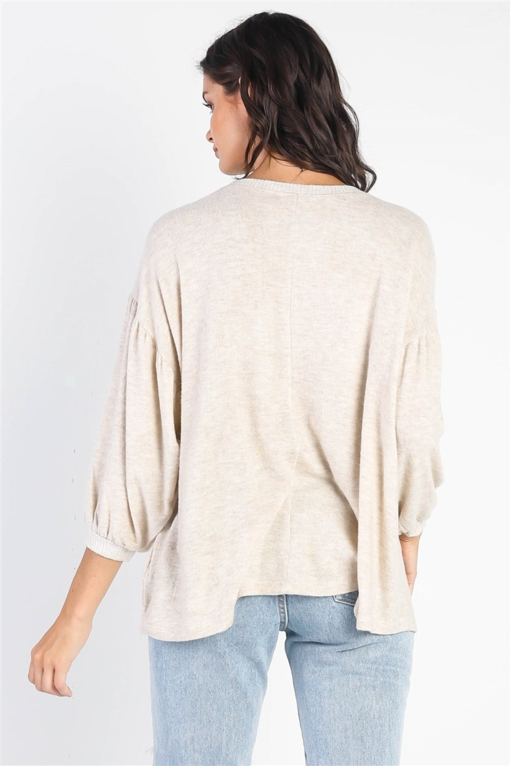 A person with long dark hair stands against a white background, smiling and raising one hand while wearing the trendy and stylish Cherish Apparel Drop Shoulder Puff Sleeve Top in burgundy paired with light blue jeans.