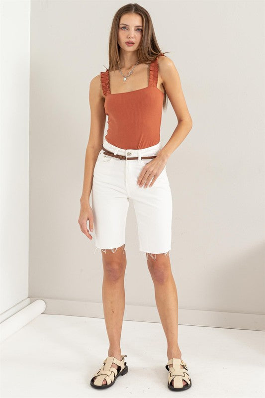 A young woman in a chic Ribbed Ruffle Strap Bodysuit and ripped denim shorts poses against a plain background.