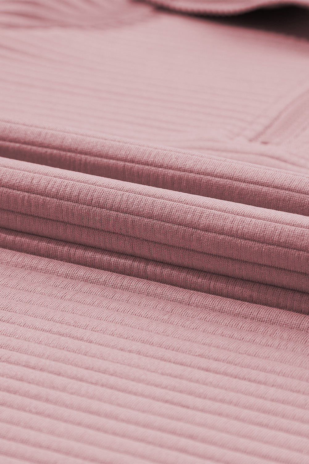 A person wearing a Peach Blossom Ribbed Texture Quarter Zip Sweatshirt and light blue jeans is standing with their back to the camera, holding a beige clutch.