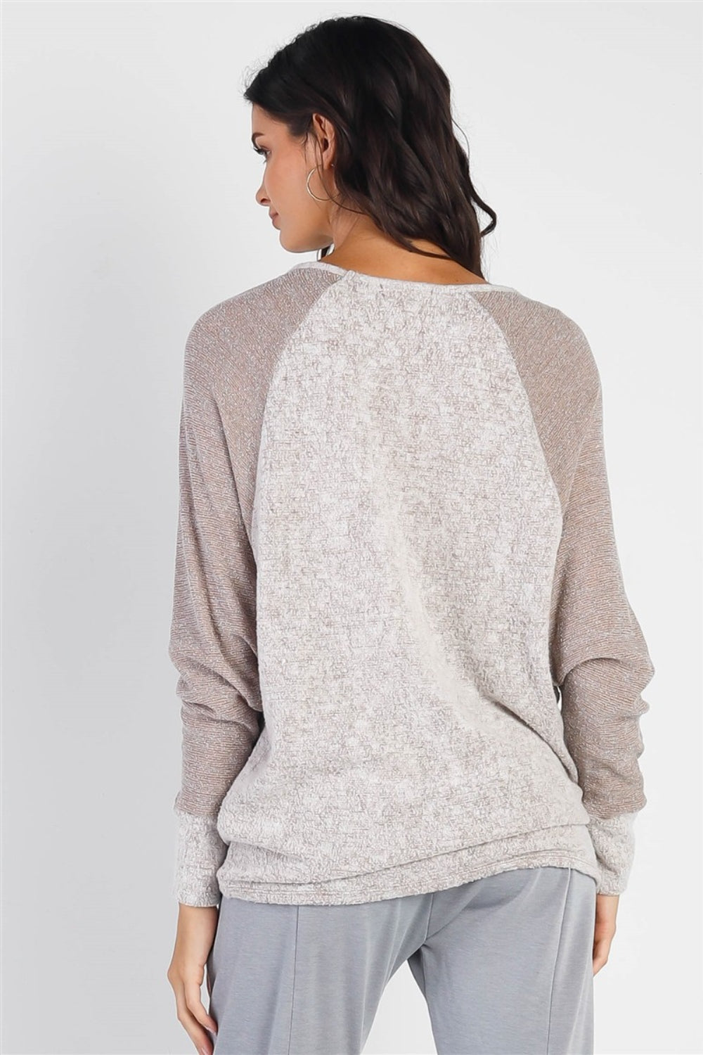 A woman stands wearing the Cherish Apparel Round Neck Long Sleeve Contrast Top in pink and gray with matching gray pants, set against a plain background.