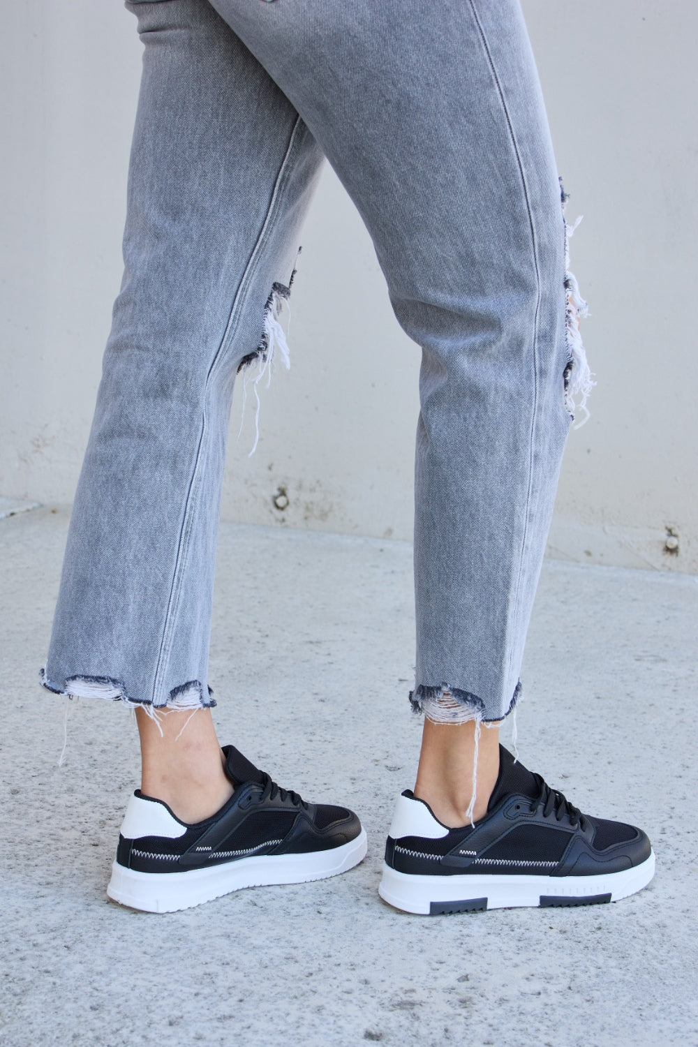 Forever Link Lace-Up Round Toe Flat Sneakers with white soles, styled with ripped gray jeans on a concrete surface.