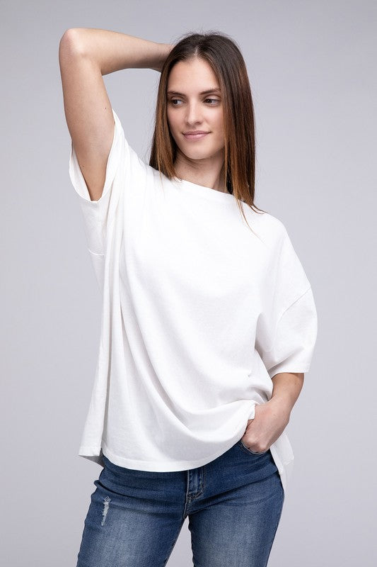 A person with long hair wearing an Oversized T-Shirt in beige with short sleeves and blue jeans, standing against a neutral background.