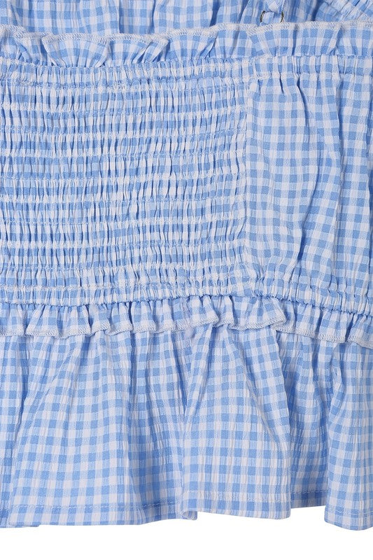 A woman wearing a Blue gingham tank top crafted from polyester spandex, paired with denim shorts, stands indoors and gazes to the side.