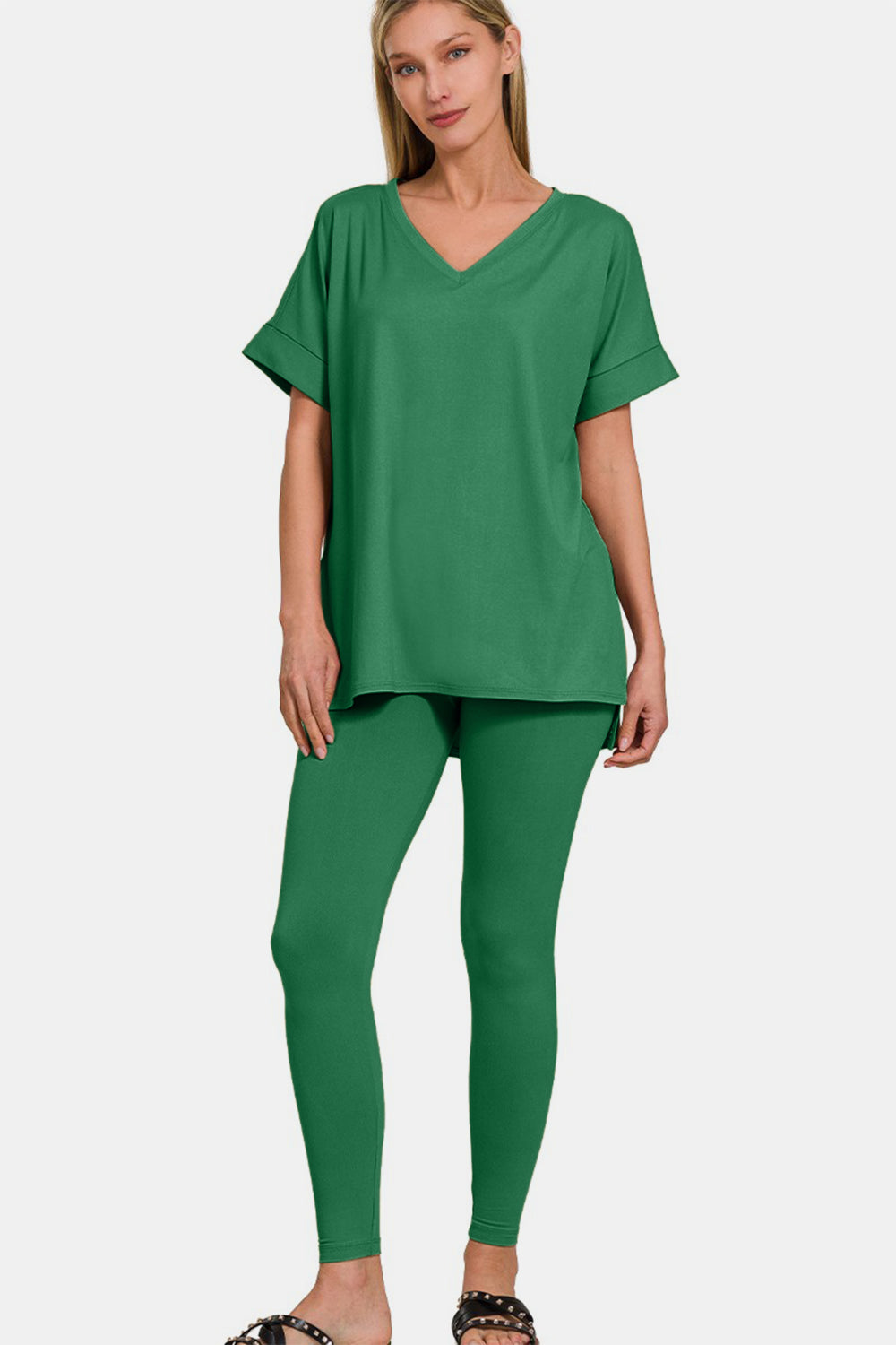 A person is modeling the Zenana Full Size V-Neck Rolled Short Sleeve T-Shirt and Leggings Lounge Set, radiating comfort and style, as they smile and stand with one hand touching their hair.