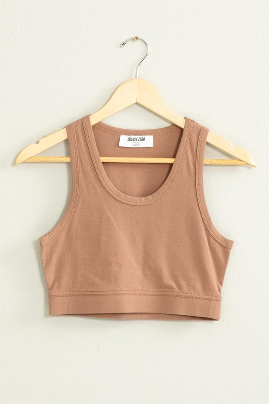 The "All I Need Cropped Tank Top," featuring a light blue hue and a fitted silhouette, hangs on a wooden hanger against a white wall.