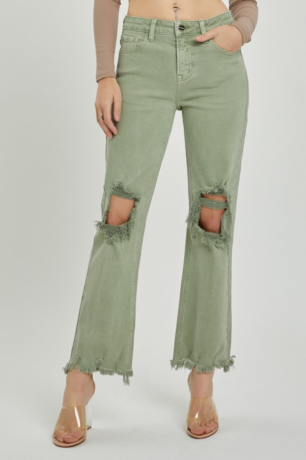 A person wearing RISEN light green distressed ankle bootcut jeans with frayed hems and a beige long-sleeved top, shown from midsection to feet.