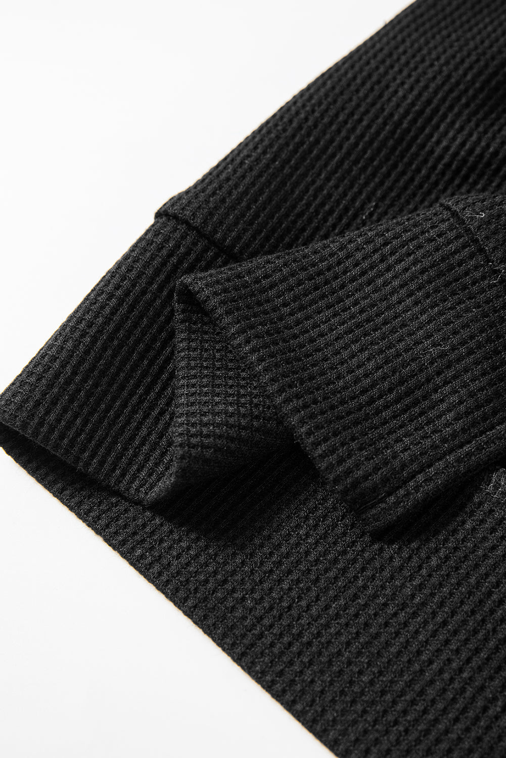 A woman wearing a Black Waffle Knit Fleece Lined High Low Oversized Hoodie and black shorts, standing and looking to the side against a plain background.