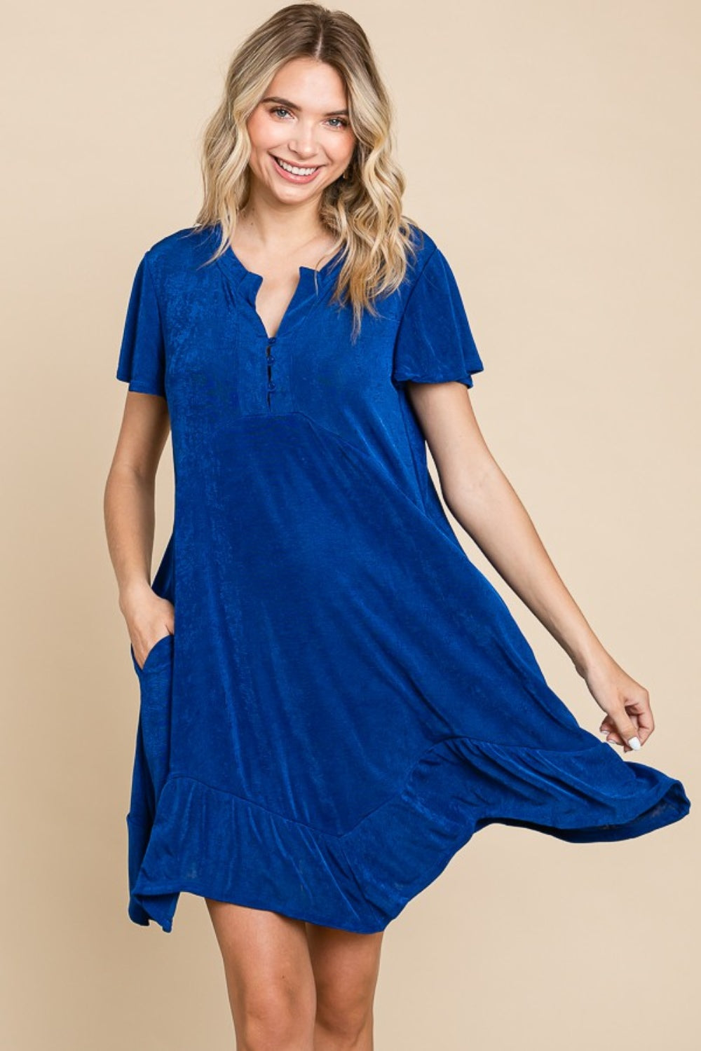 A woman wearing the Culture Code Full Size Short Sleeve Ruffled Asymmetric Hem Dress poses against a beige background.