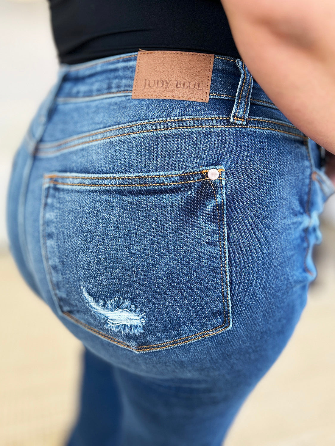 Person standing indoors wearing Judy Blue Full Size Mid Rise Distressed Raw Hem Jeans and black sneakers.