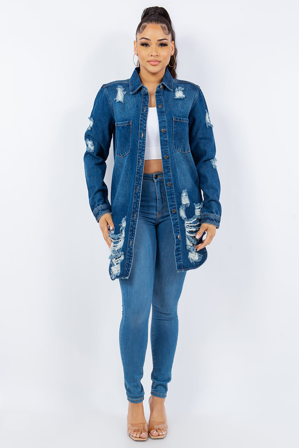 A woman is wearing an American Bazi Distressed Button Up Long Sleeve Denim Jacket over a white top and distressed jeans, posing against a plain background. The denim jacket adds an edgy touch to her chic ensemble.