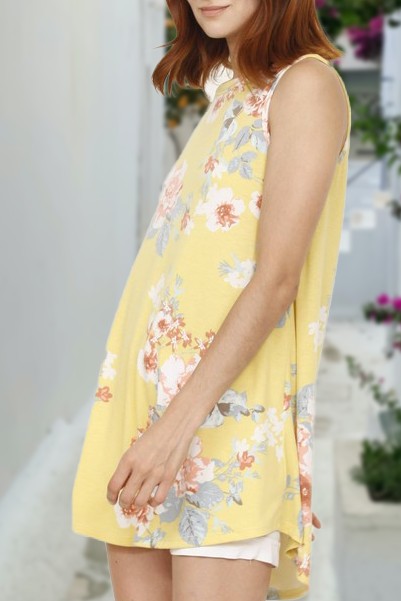 A woman wearing a Floral Tank Top with a yellow floral print stands outdoors near a white wall and plants.