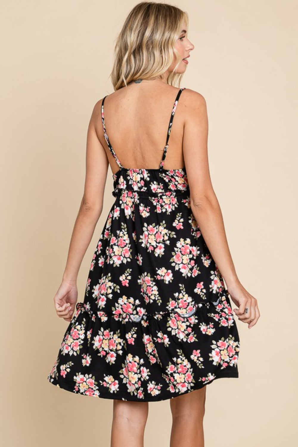 A woman poses against a beige background, modeling the Culture Code Full Size Floral Frill Cami Dress, featuring a black floral print and delicate frilled detailing at the hem.