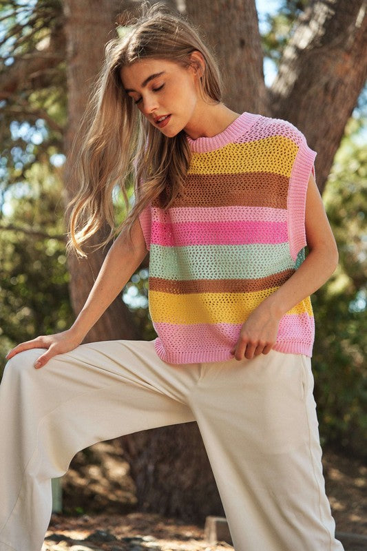 A woman outdoors wearing a Crochet Multi Striped Pullover Knit Sweater Vest and white pants, with her arms raised and eyes closed.