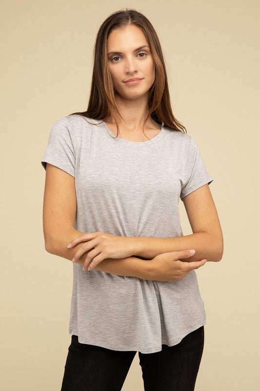 A person with long hair is wearing a blue Flowy Round Hem Rayon Short Sleeve Top and black pants, standing against a plain beige background.