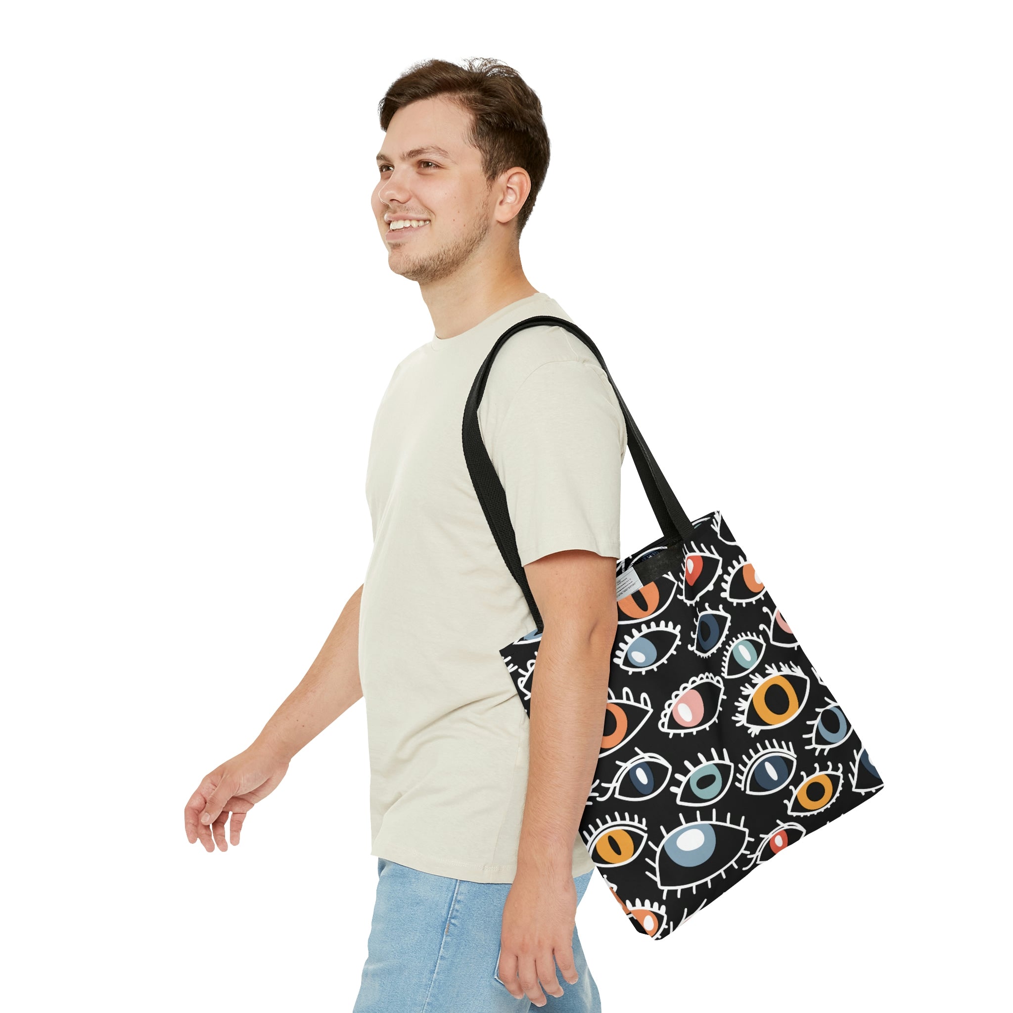 A shopping tote bag featuring a pattern of stylized Egyptian eyes in various colors and designs on a black background, complete with black cotton handles.
