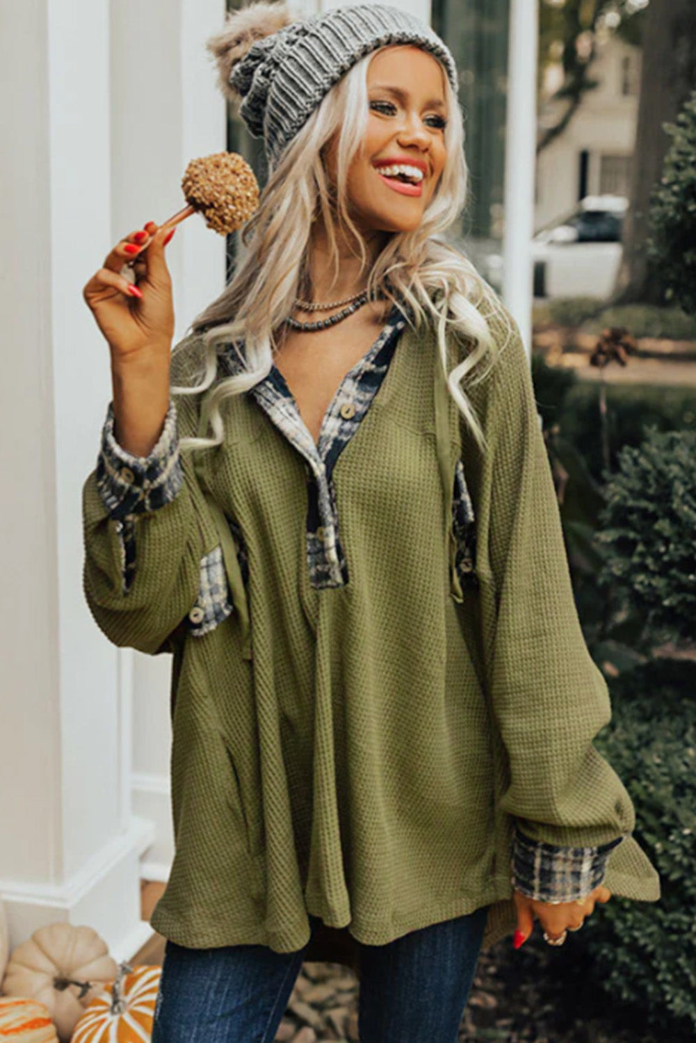 A person wearing a grey beanie, the Green Flowy Plaid Accent Waffle Knit Henley Hoodie, and a plaid shirt is standing outside next to a pumpkin and greenery.