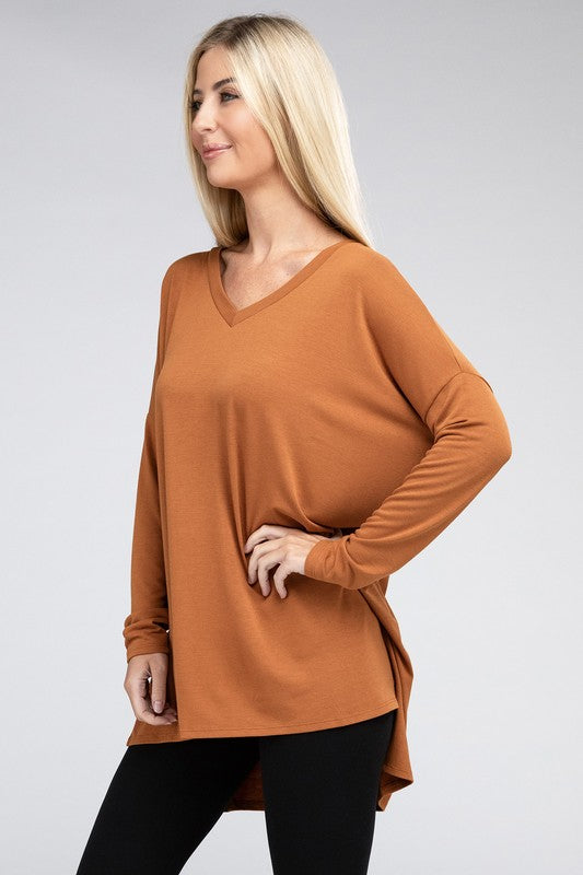 A woman with long, blonde hair is wearing a loose-fitting, brown Dolman Long Sleeve V-Neck Side Slit Hi-Low Hem Top and black pants. She poses with one hand on her hip and a neutral facial expression against a light grey background.