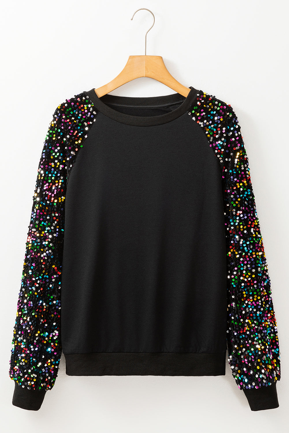 A person with long dark hair stands in front of a decorated Christmas tree, wearing a Black Sequin Raglan Sleeve Crewneck Pullover Sweatshirt.