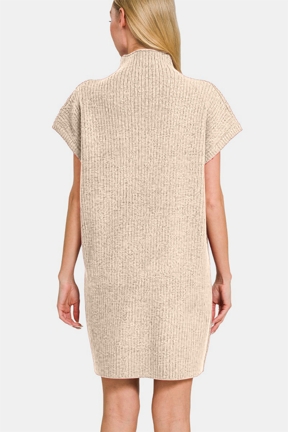 A woman is posing against a white background while wearing the Zenana Short Sleeve Sweater Mini Dress, a beige, ribbed mini dress with short sleeves and a high neck. It features a front pocket and effortlessly combines style and function.