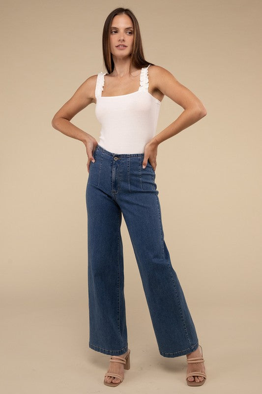 A young woman in a chic Ribbed Ruffle Strap Bodysuit and ripped denim shorts poses against a plain background.