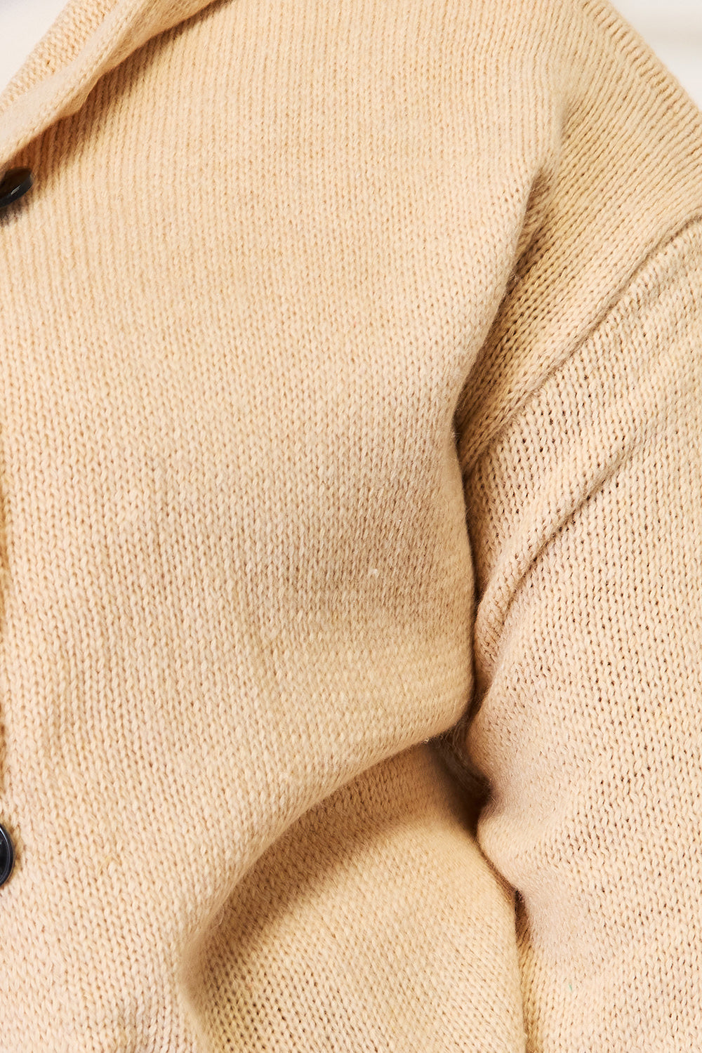 A person stands in a well-lit room wearing the Woven Right Button-Down Long Sleeve Hooded Sweater in a cream color over a white top and brown pants. The individual smiles slightly and poses with one hand in a pocket, against a light background.