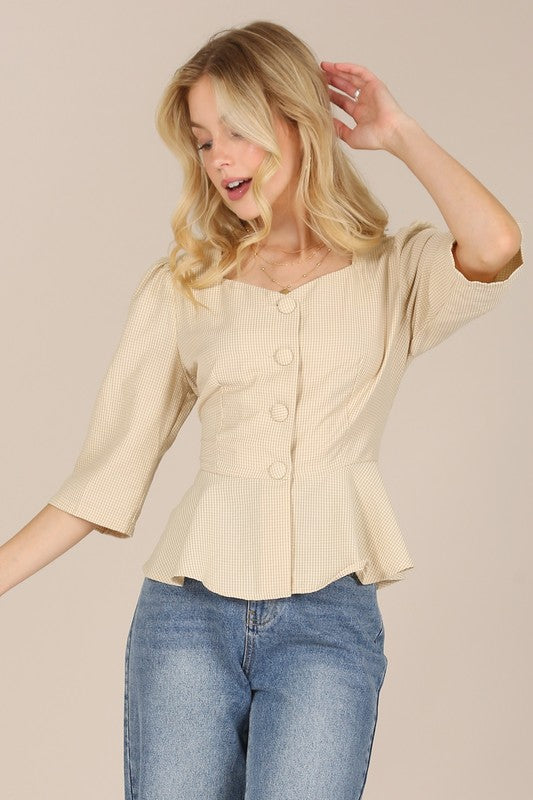 A person with long blonde hair is posed against a plain background, wearing a beige 3/4 sleeve front button blouse paired with puff sleeves and blue jeans.