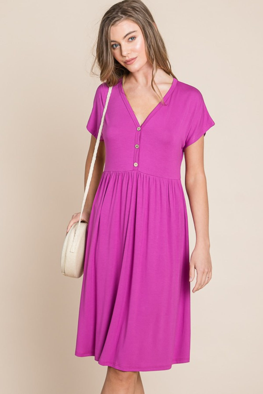 A person stands against a neutral background wearing the BOMBOM V-Neck Short Sleeve Dress, featuring a vibrant pink color and button details, crafted from soft rayon spandex fabric.