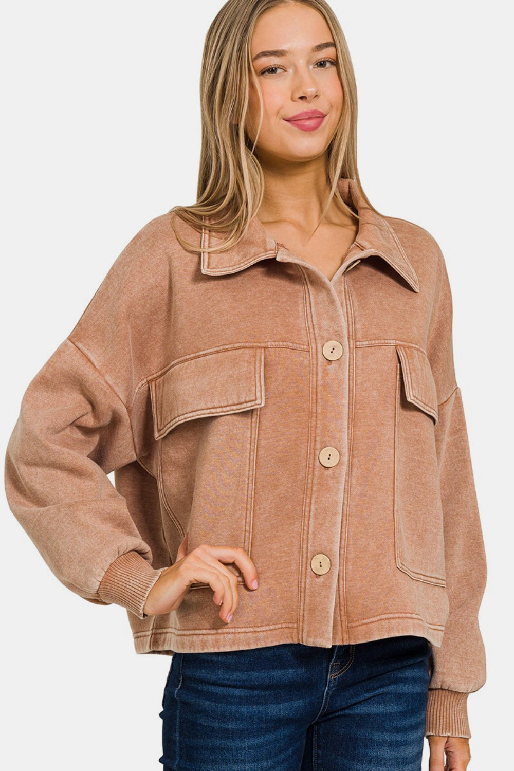 A person wearing the Zenana Wash Fleece Front Pocket Button Up Shacket in tan and blue jeans poses stylishly against a plain background.