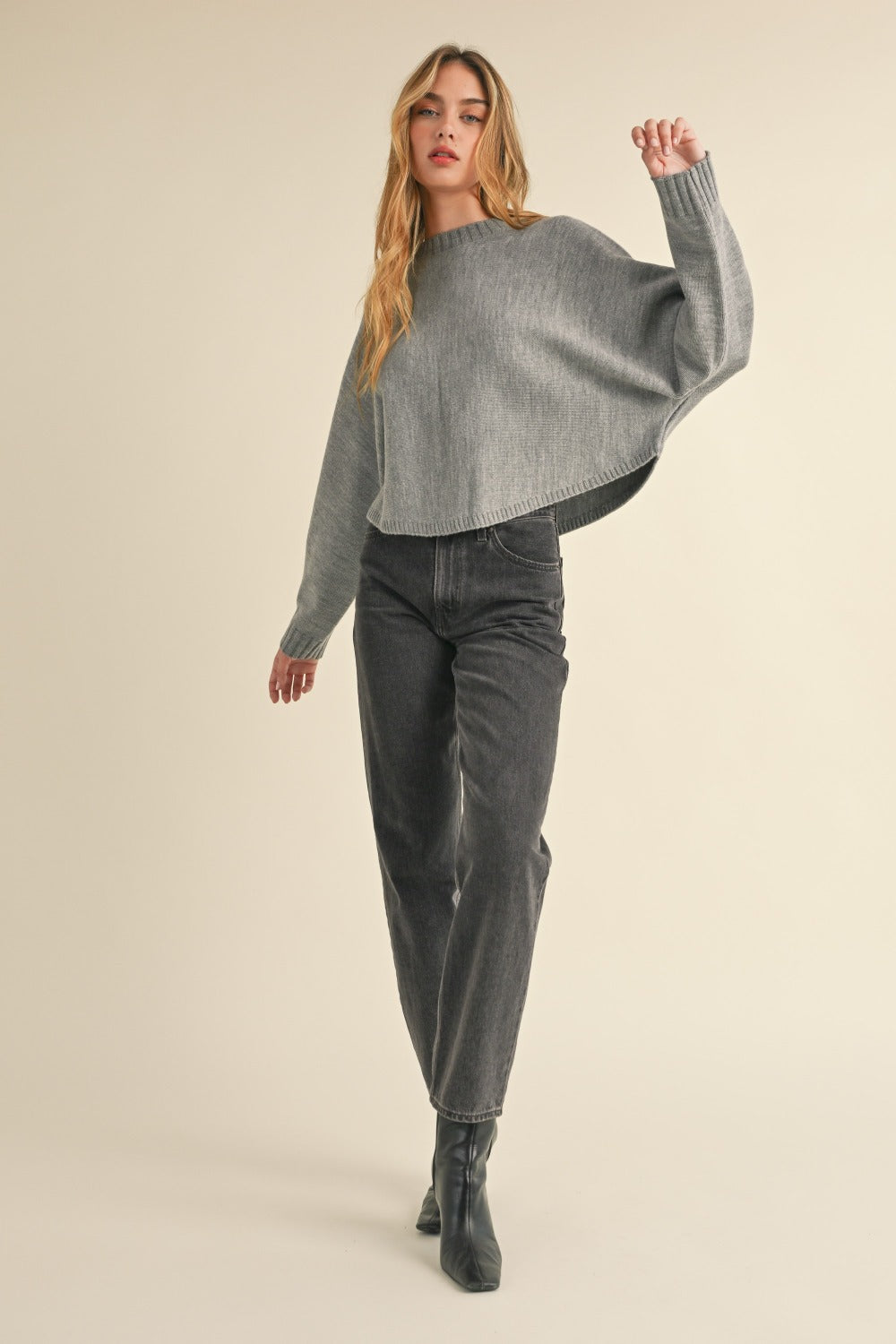 A person with long, light brown hair is facing away, wearing a Mable Round Neck Dolman Sleeve Cropped Sweater in grey paired with dark jeans, against a neutral background.