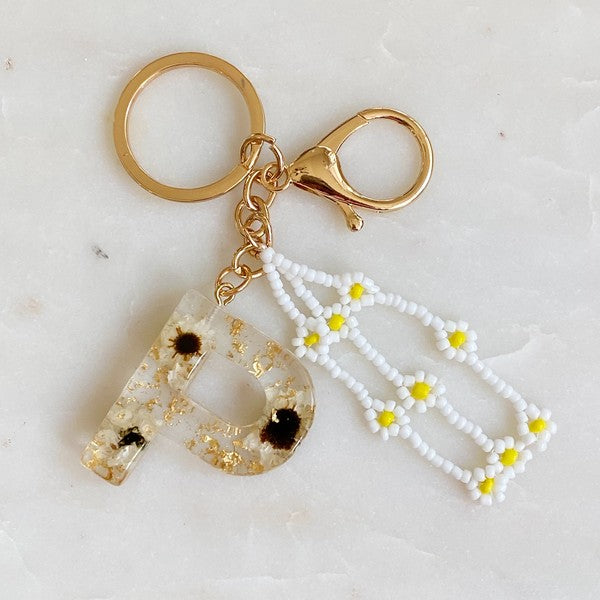 Baby Daisy Initial Key Chain alphabet keychains with real daisy flowers and gold flakes on a marble surface.