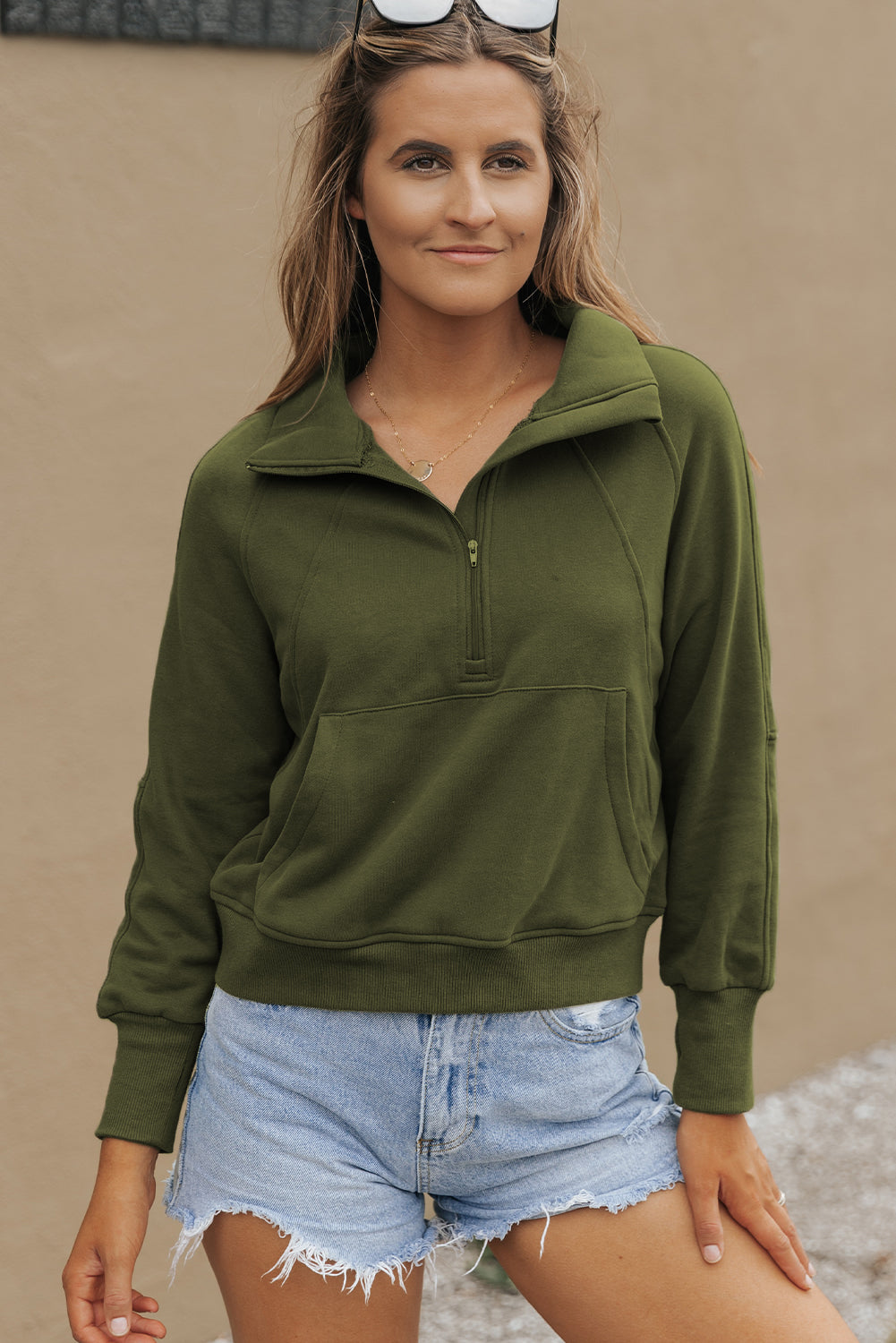 A person with long, wavy hair stands in front of a white and black background, wearing the Green Fleece Lined Zip Up Stand Collar Thumbhole Sleeve Sweatshirt paired with white shorts, creating a stylish look perfect for casual outings.