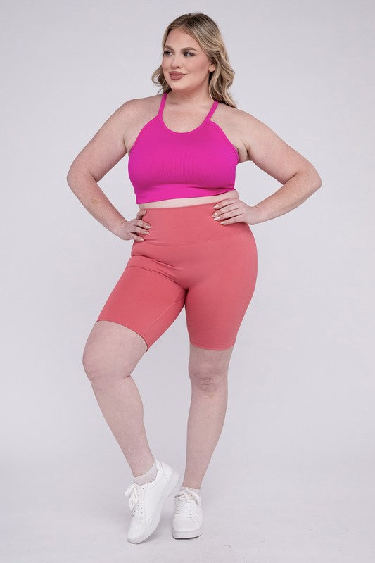 Against a plain background, a person showcases the Plus Athletic High Rise Biker Shorts in coral, crafted from high-quality athletic fabric and paired with a pink top.