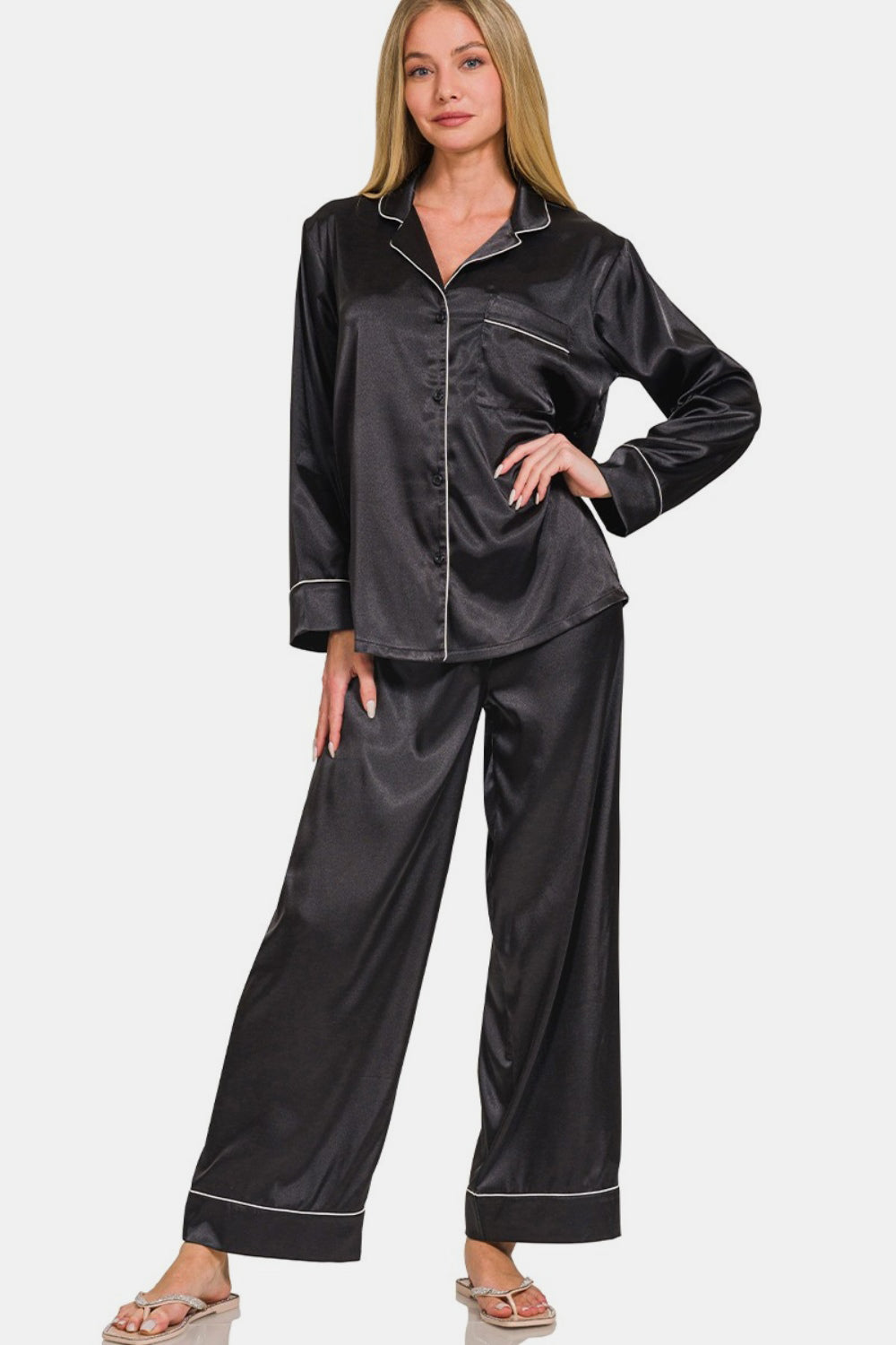 A person wearing the Zenana Satin Long Sleeve Shirt and Pants Pajama Set in black with white piping stands in a relaxed pose.