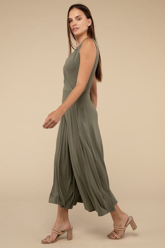 A woman stands in a studio, wearing an elegant olive green Surplice Neckline Sleeveless Jumpsuit with wide legs and paired with beige heels.