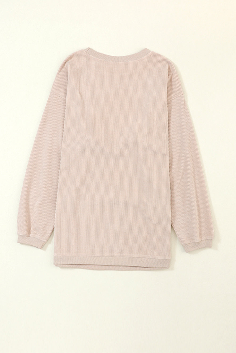 A woman stands outdoors, looking down while touching her hair with one hand. She is wearing an Apricot Ribbed Corduroy Oversized Sweatshirt and white pants, exuding an effortlessly chic and fashionable look.