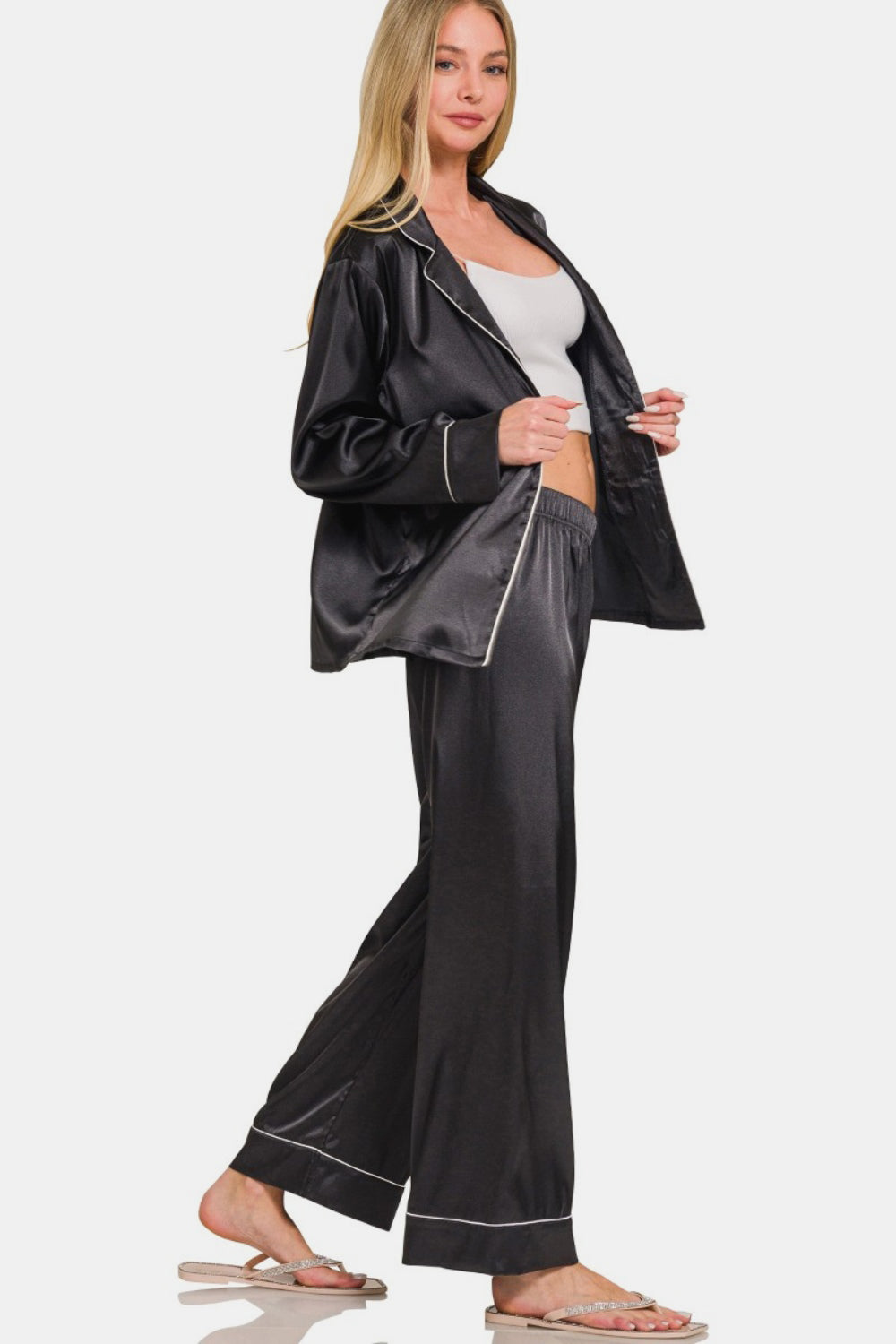 A person wearing the Zenana Satin Long Sleeve Shirt and Pants Pajama Set in black with white piping stands in a relaxed pose.