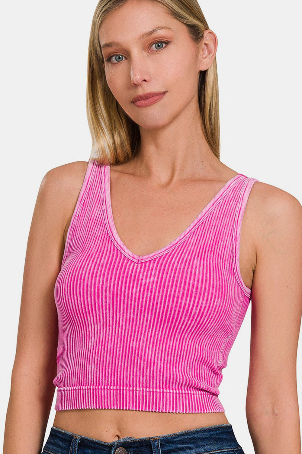 A person wearing the Zenana Washed Ribbed Cropped Bra Padded Tank in a stylish pink stands against a white background, showcasing the comfort of their wardrobe choice.