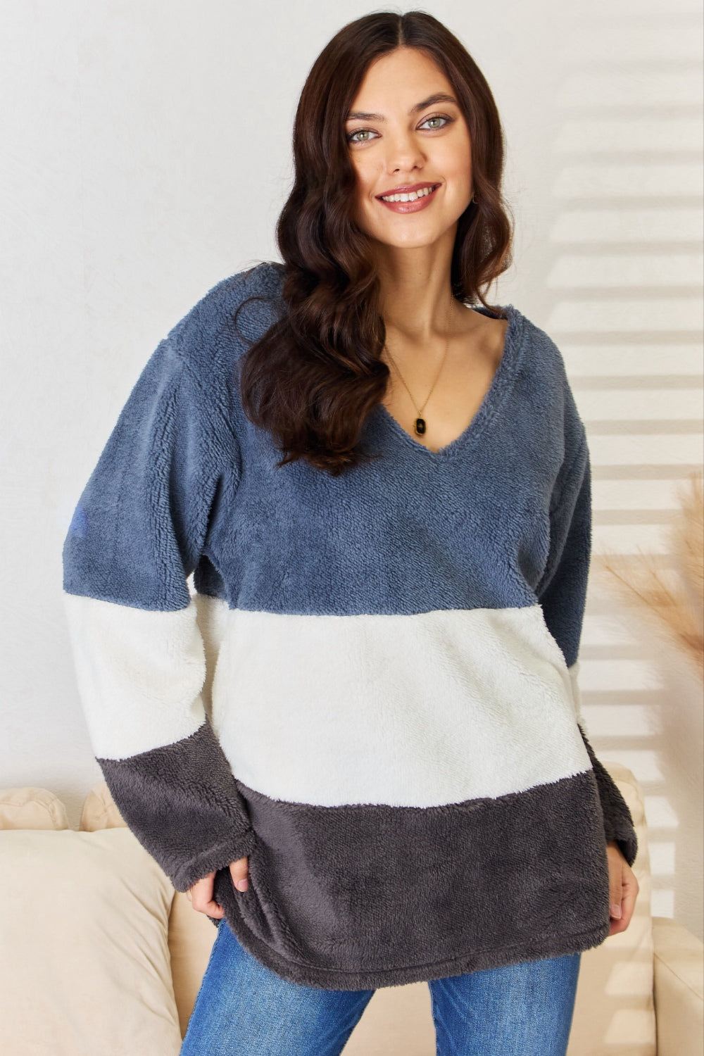 A woman with long, dark hair smiles while wearing the Culture Code Faux Fur Color Block V-Neck Sweater in shades of navy, white, and gray, paired with blue jeans—a versatile wardrobe addition.