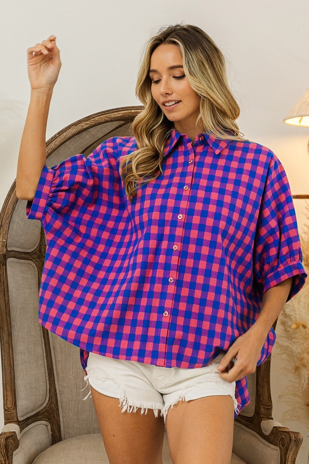 Person wearing a BiBi Plaid Button Up Dolman Sleeve Shirt in blue and pink with white shorts, standing in front of a wooden chair.