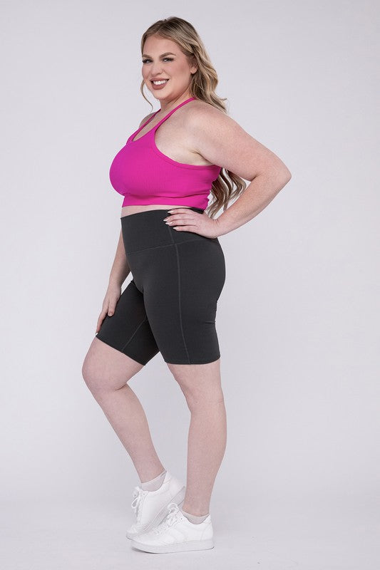 Against a plain background, a person showcases the Plus Athletic High Rise Biker Shorts in coral, crafted from high-quality athletic fabric and paired with a pink top.